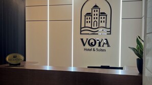 A reception desk with a sign for VOYA Hotel & Suites, a reception area, and a security camera. - Voya Hotel and Suites (Tyre)