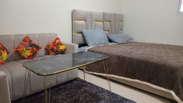 A bedroom with a grey sofa, colorful pillows, a small black table, and a large bed with a brown blanket. - Clean & Cozy Room in Aïn Chock, Casa Nearshore casablanca (casablanca)