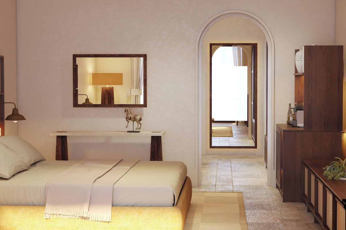 Ein Schlafzimmer mit Bett, Nachttisch, Spiegel und Blick durch einen Bogen in einen anderen Raum.