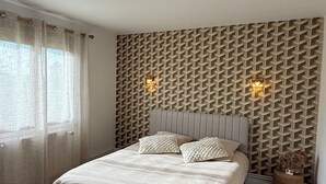 A bedroom with a bed, a patterned rug, a wall with geometric patterns, and two wall-mounted lights. - Cosy house in Moyvillers (Moyvillers)