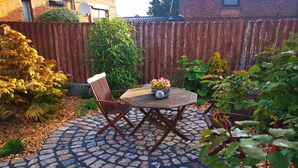 A circular patio with a wooden table and chairs, surrounded by a stone-patterned walkway. - Apartment Beautiful View (Usedom)