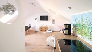 A modern kitchen with a coffee maker, a dining area with a white table and chairs, and a TV mounted on the wall. - Apartment Beautiful View (Usedom)
