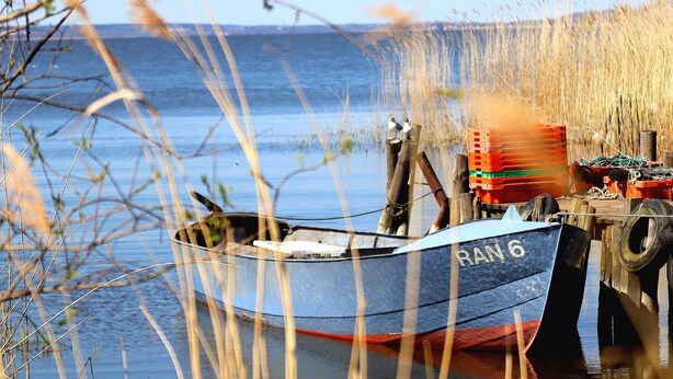 Una embarcación llamada "RAN 6" atracada en un muelle, con vista despejada al agua y la costa lejana.