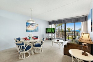 Ein Hotelzimmer mit Essbereich, Fernseher, Sofa und Blick auf den Ozean.