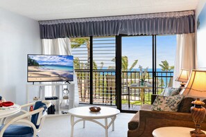Ein Hotelzimmer mit Balkon, Fernseher, Esstisch und einer Couch.