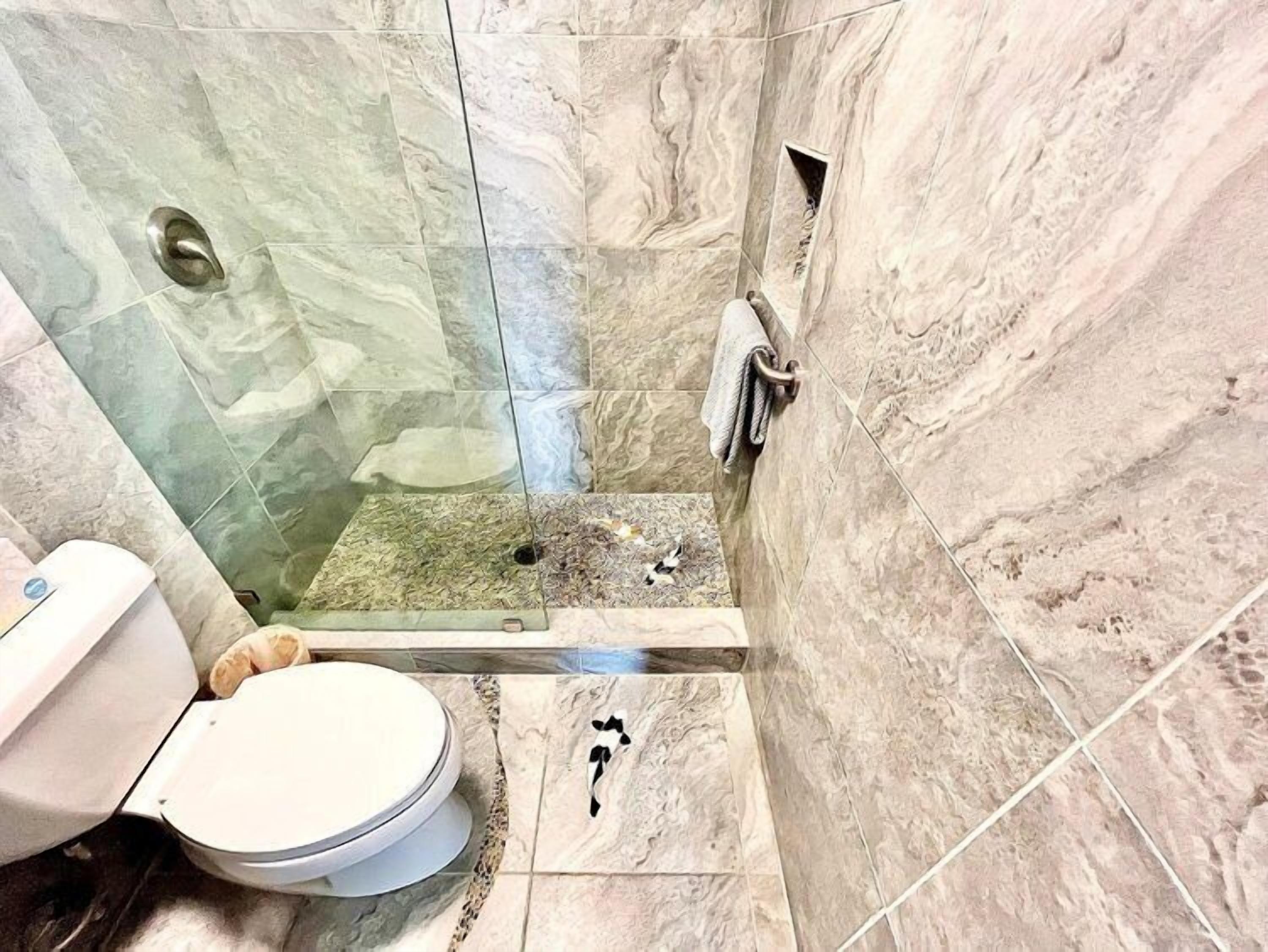 A bathroom with a glass shower enclosure, a toilet, and a marble-tiled wall.