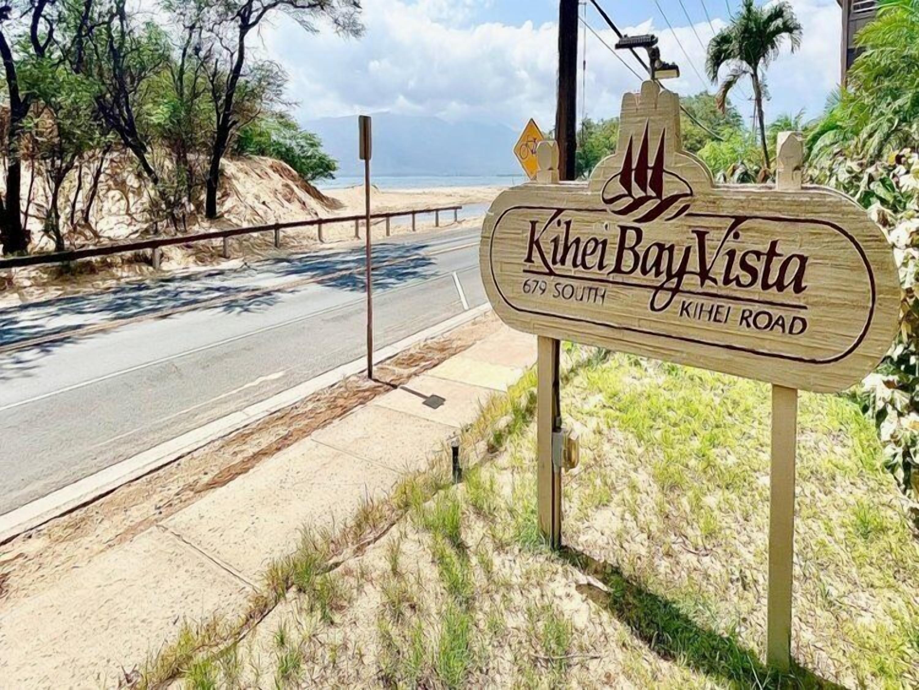 A wooden sign for Kihei Bay Vista on Kihei Road, indicating the location.