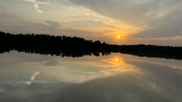 A calm lake reflecting the sunset with a forested horizon.