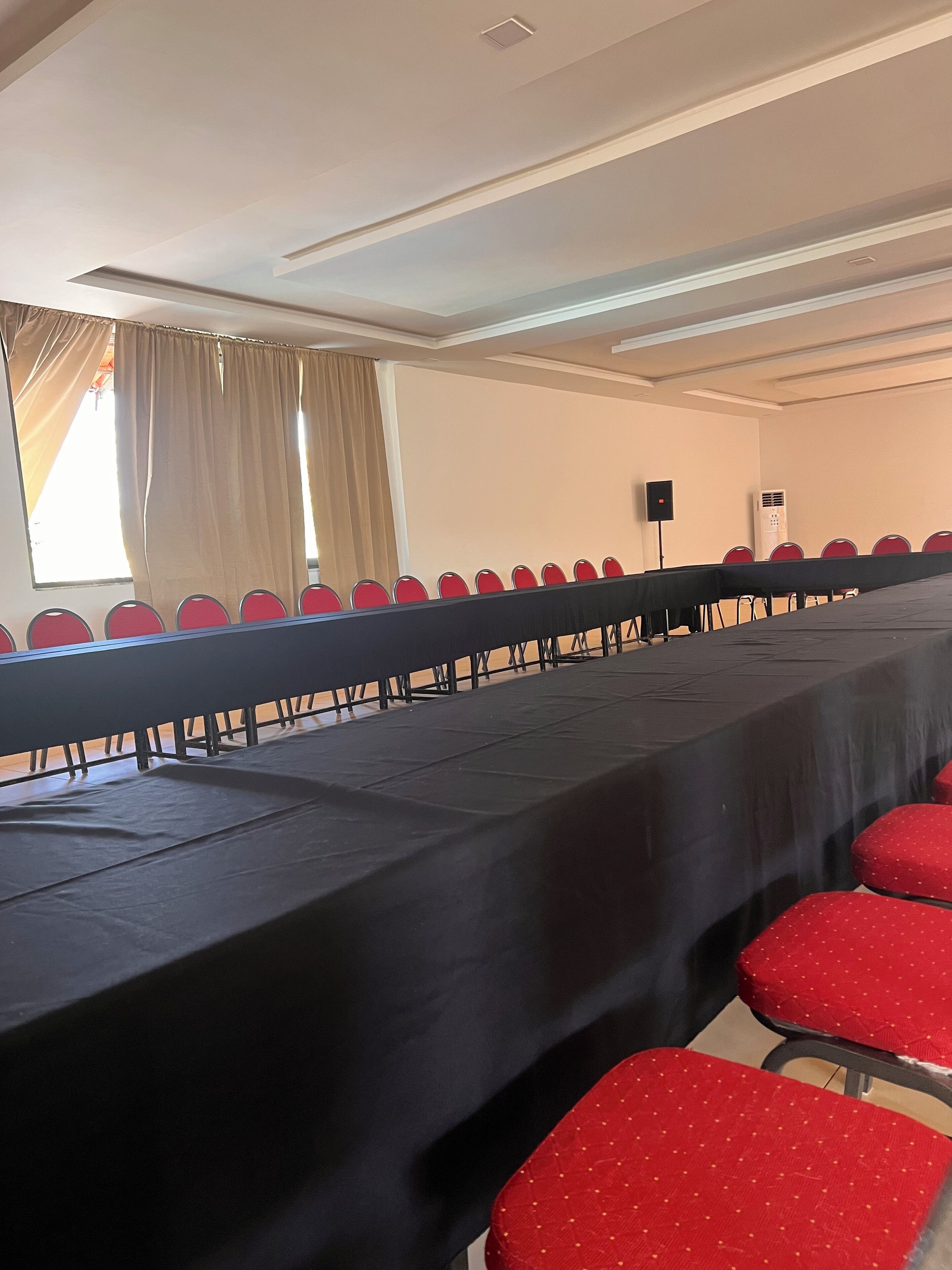 Un salón de conferencias con una larga mesa, sillas rojas, un orador y un equipo de aire acondicionado.