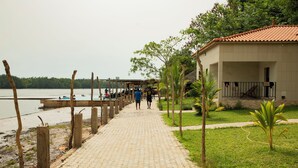 A paved walkway leading to a building with a tiled roof, surrounded by greenery and a body of water.
