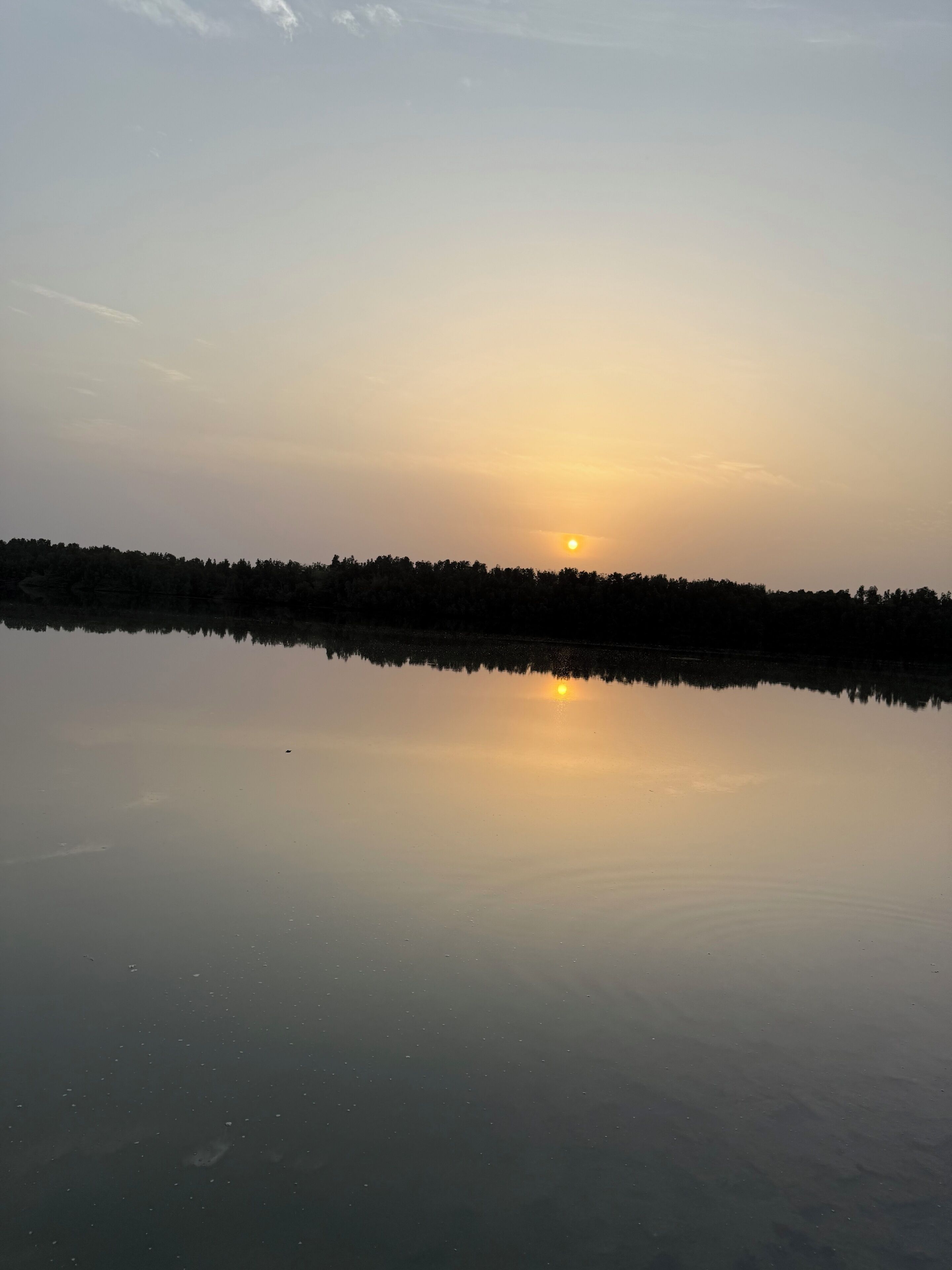 A calm lake reflecting the sunset with a forested horizon.
