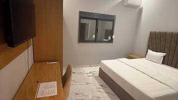 Quarto moderno com cama, escrivaninha, cadeira, televisão e janela.