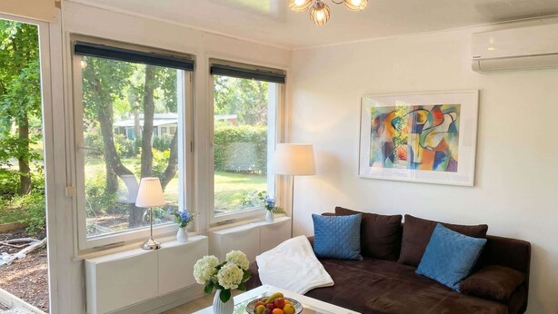 Un salon moderne avec un canapé marron, une table basse blanche sur laquelle se trouve un panier de fruits, et un tableau accroché au mur.