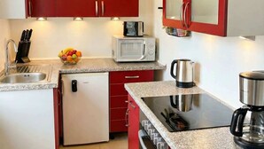 Une cuisine compacte avec des meubles rouges, un four à micro-ondes, une machine à café et un lave-vaisselle.