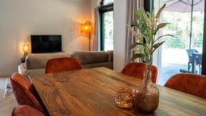 A dining area with a wooden table, red upholstered chairs, a vase with a plant, and a television in the background. - Ecovilla With Forest View for 6 Person (Oirschot)