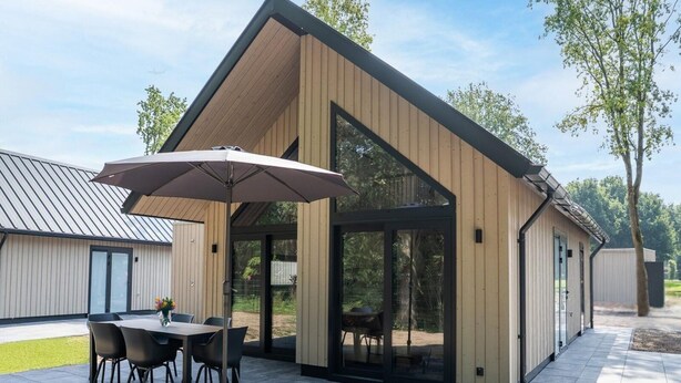 A modern building with a patio area featuring a table and chairs, a large umbrella, and a glass enclosure. - Ecovilla With Forest View for 6 Person (Oirschot)