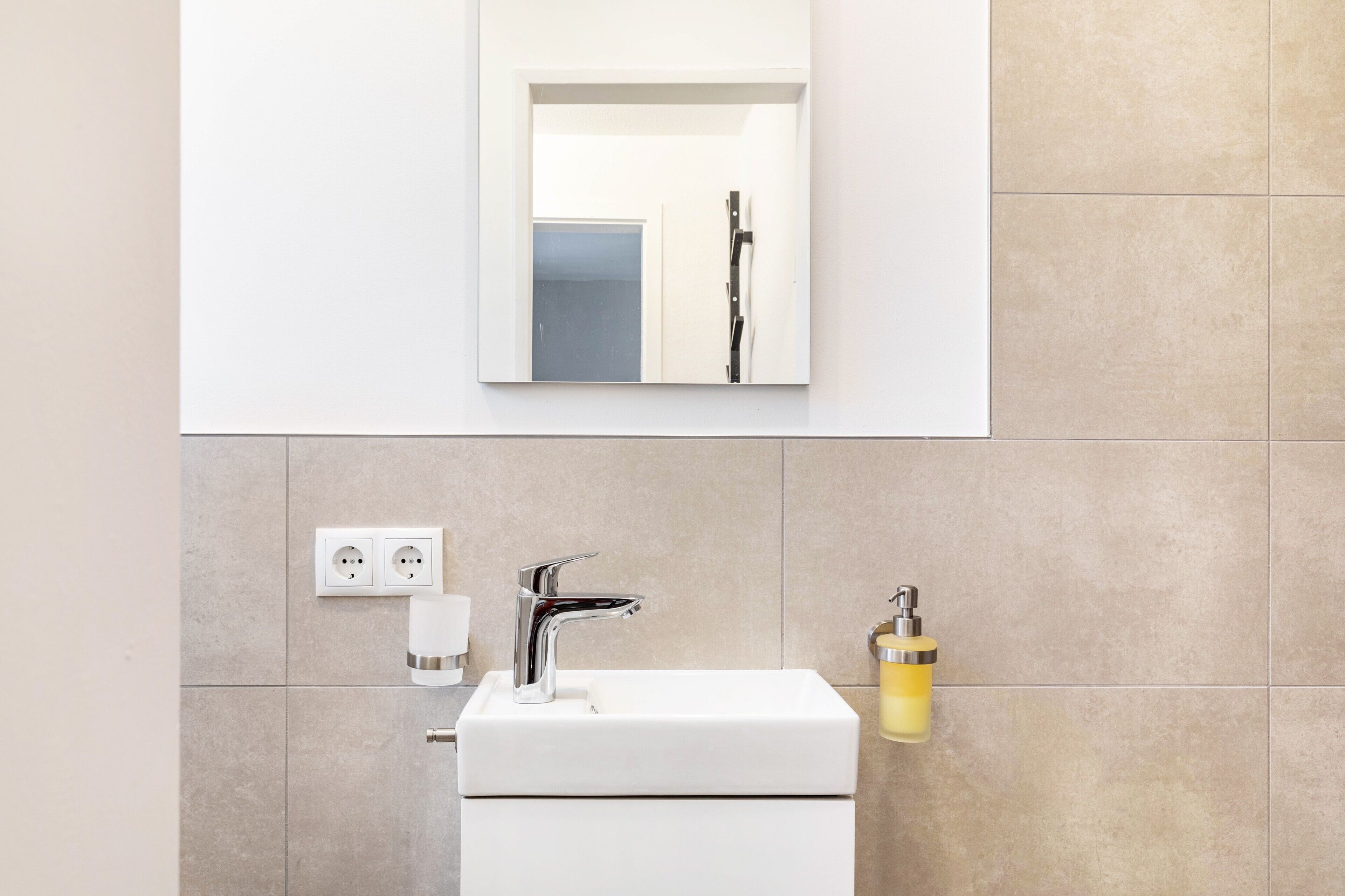 Une salle de bain avec un lavabo blanc, un miroir et un distributeur de savon jaune.