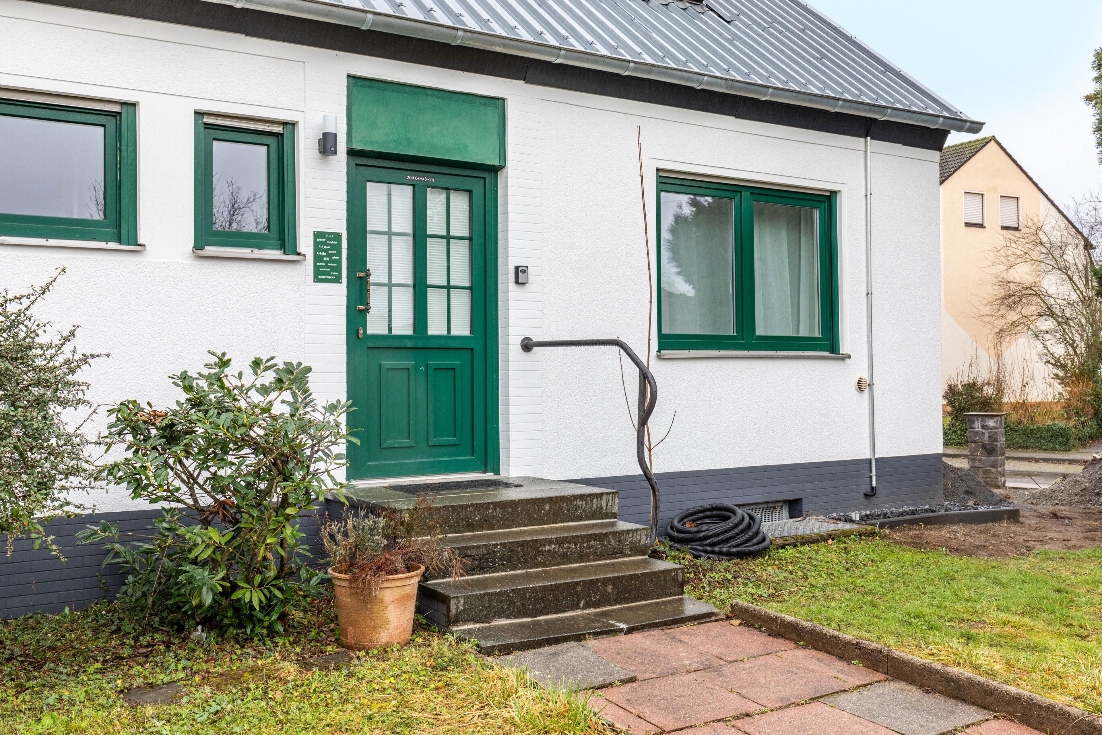 Un edificio bianco con una porta e finestre verdi, un piccolo giardino e una serie di gradini che conducono all'ingresso.