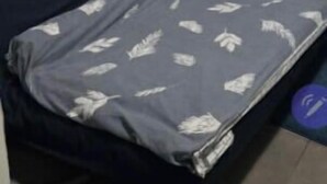 Une chambre à coucher avec un lit, une étagère ornée d’un vase de fleurs et un tableau d’affichage accroché au mur.