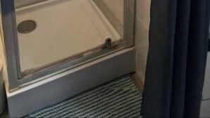 Une cabine de douche fermée par des parois en verre, dotée d’un pommeau de douche à main, d’un robinet mural et d’une petite étagère.
