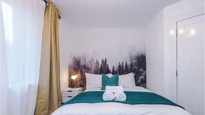 A neatly made bed with white linens and a green accent, a nightstand with a lamp, and a forest-themed wall mural. - Business Travellers & Couples with Free Parking (Salford)