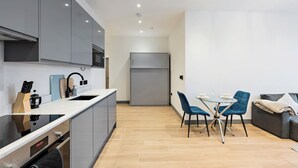 Una cocina moderna con gabinetes grises, un horno empotrado y un microondas. Hay una zona de comedor con una mesa de vidrio y sillas azules.