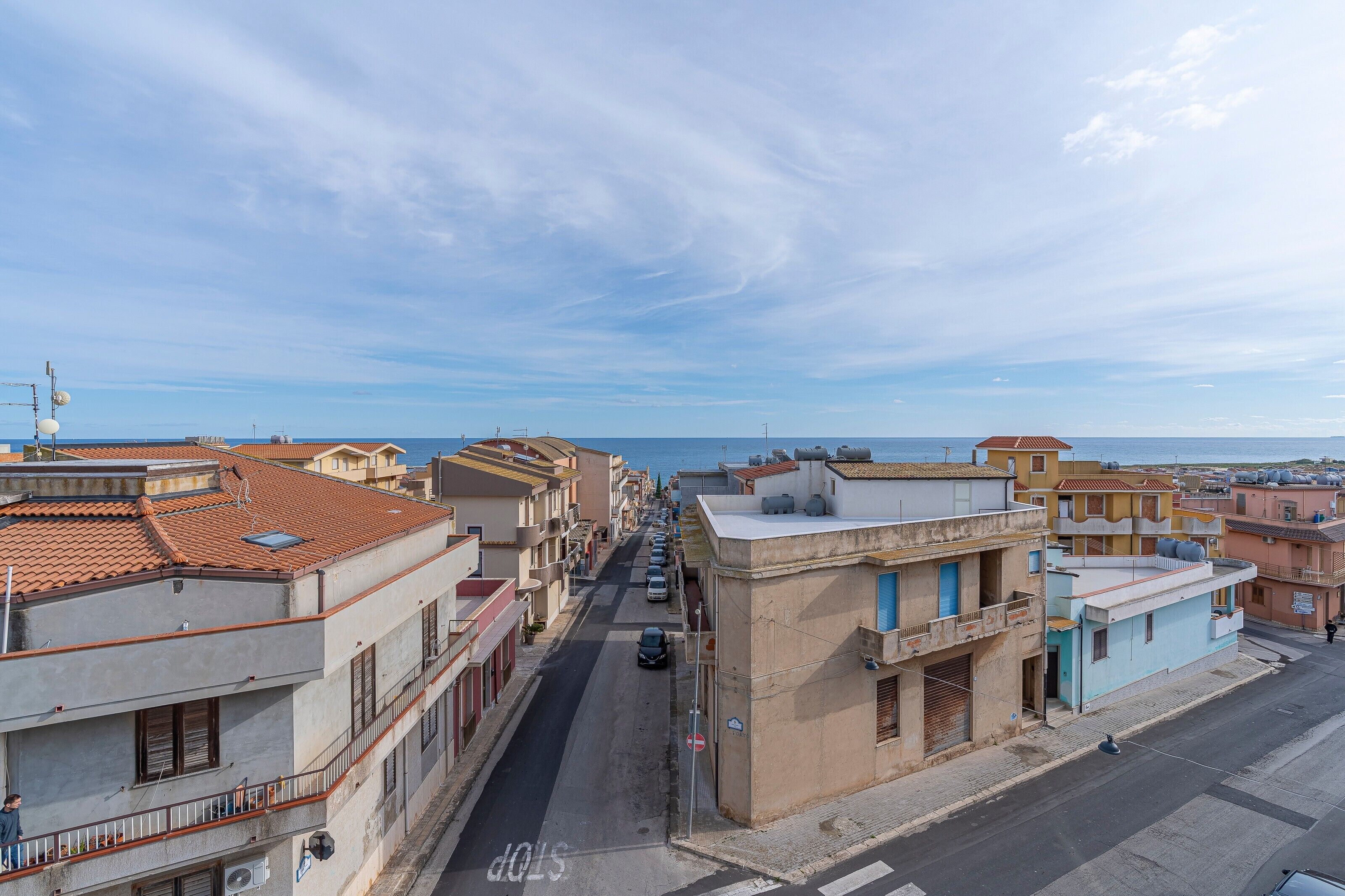 Un carrer marítim amb edificis, un cel serè i el mar a la distància.