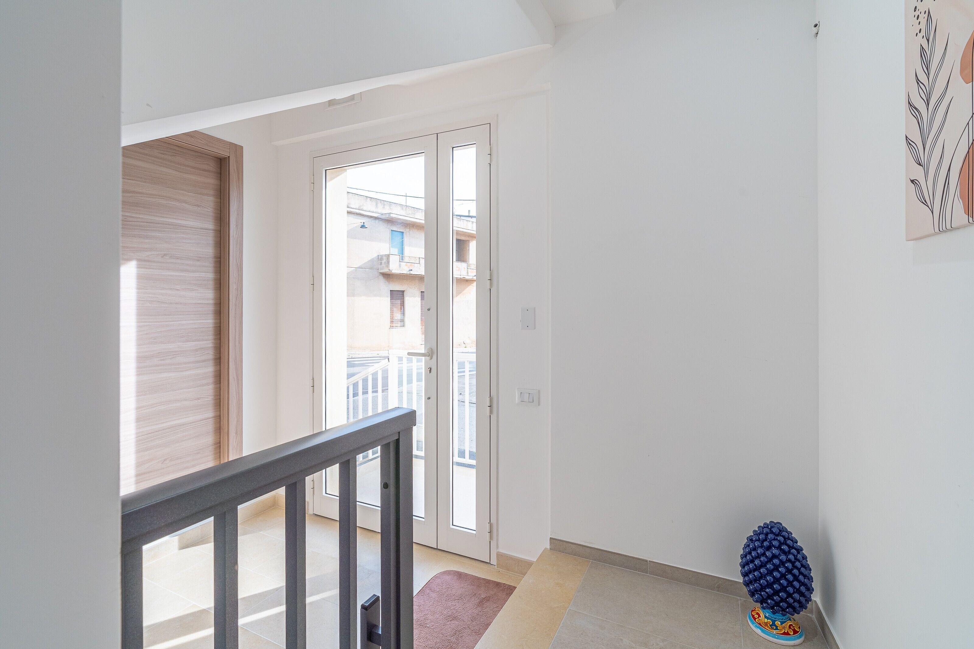 Un pasillo con una puerta de madera, una puerta de cristal que da al exterior, y un pequeño adorno en el suelo.