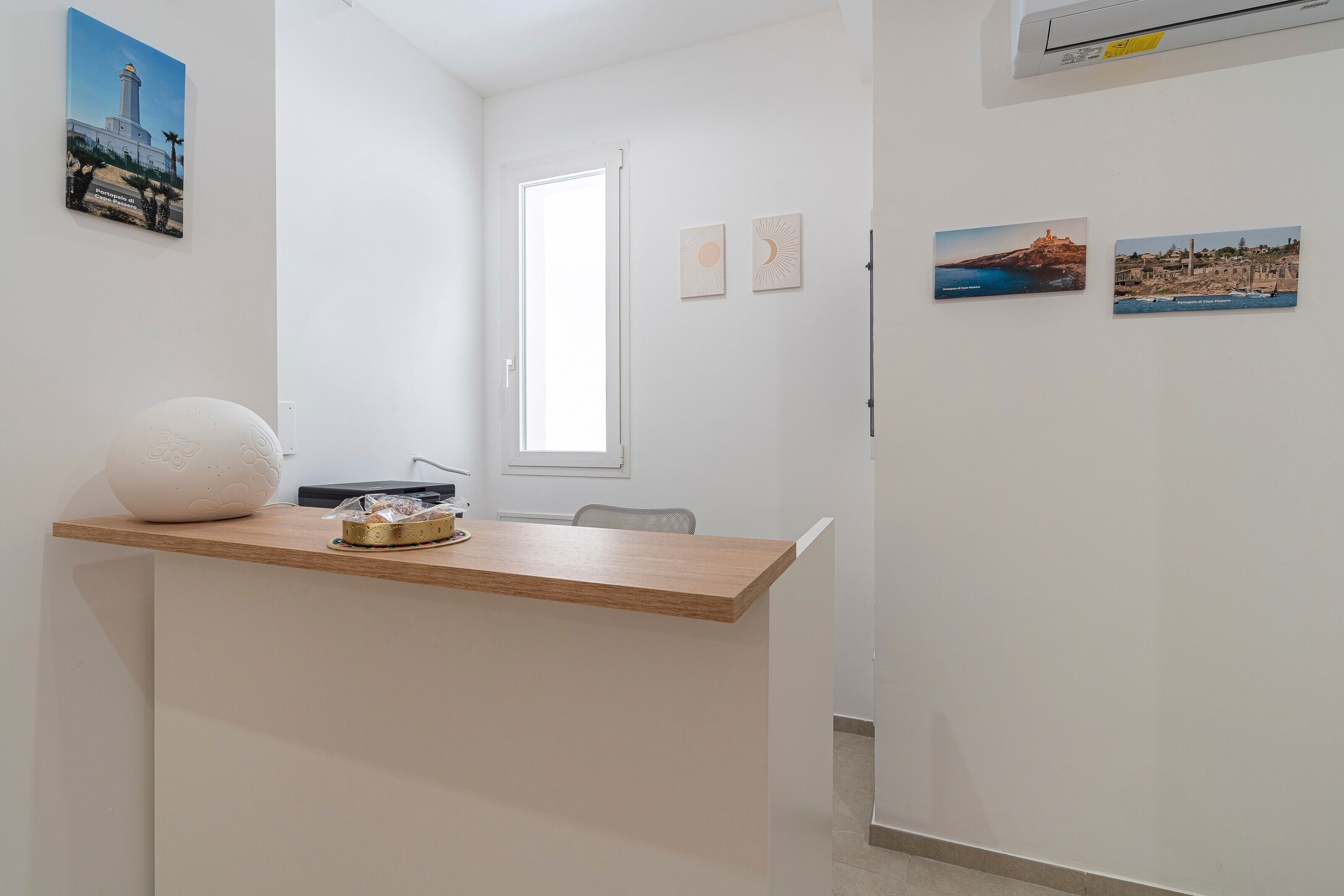 Ein helles, modernes Hotelzimmer mit einem Holzbüro, einer weißen Vase und einem kleinen Tisch mit Tablett. An der Wand hängen zwei gerahmte Bilder, ein Fenster und eine Tür.