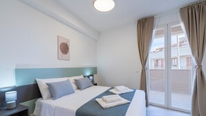 Een hotelkamer met een bed, nachtkastjes, een raam met gordijnen en uitzicht op gebouwen.