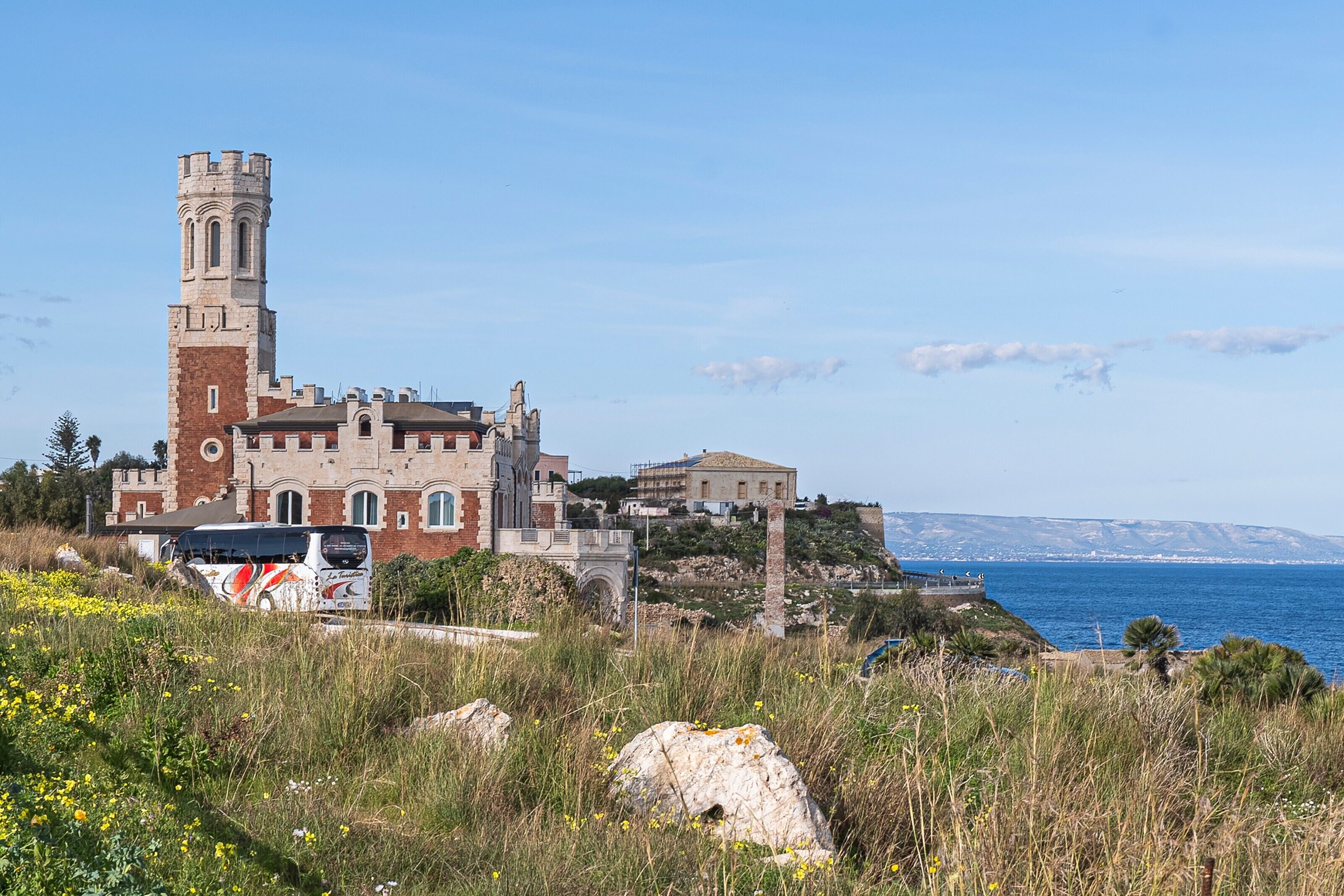 A historic building with a tower, situated on a coastal cliff with a view of the sea.