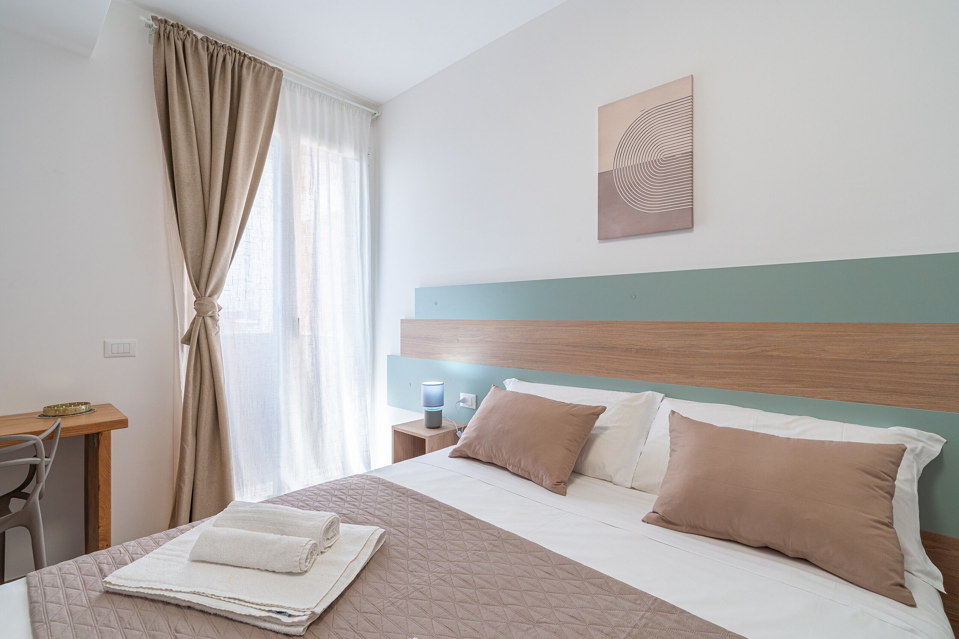 Un lit bien fait, recouvert d’une courtepointe matelassée, une table de chevet avec une lampe, une chaise et une fenêtre avec des rideaux.