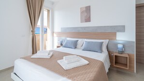 Et hotelværelse med seng, natbord, væglampe og et vindue med gardiner.