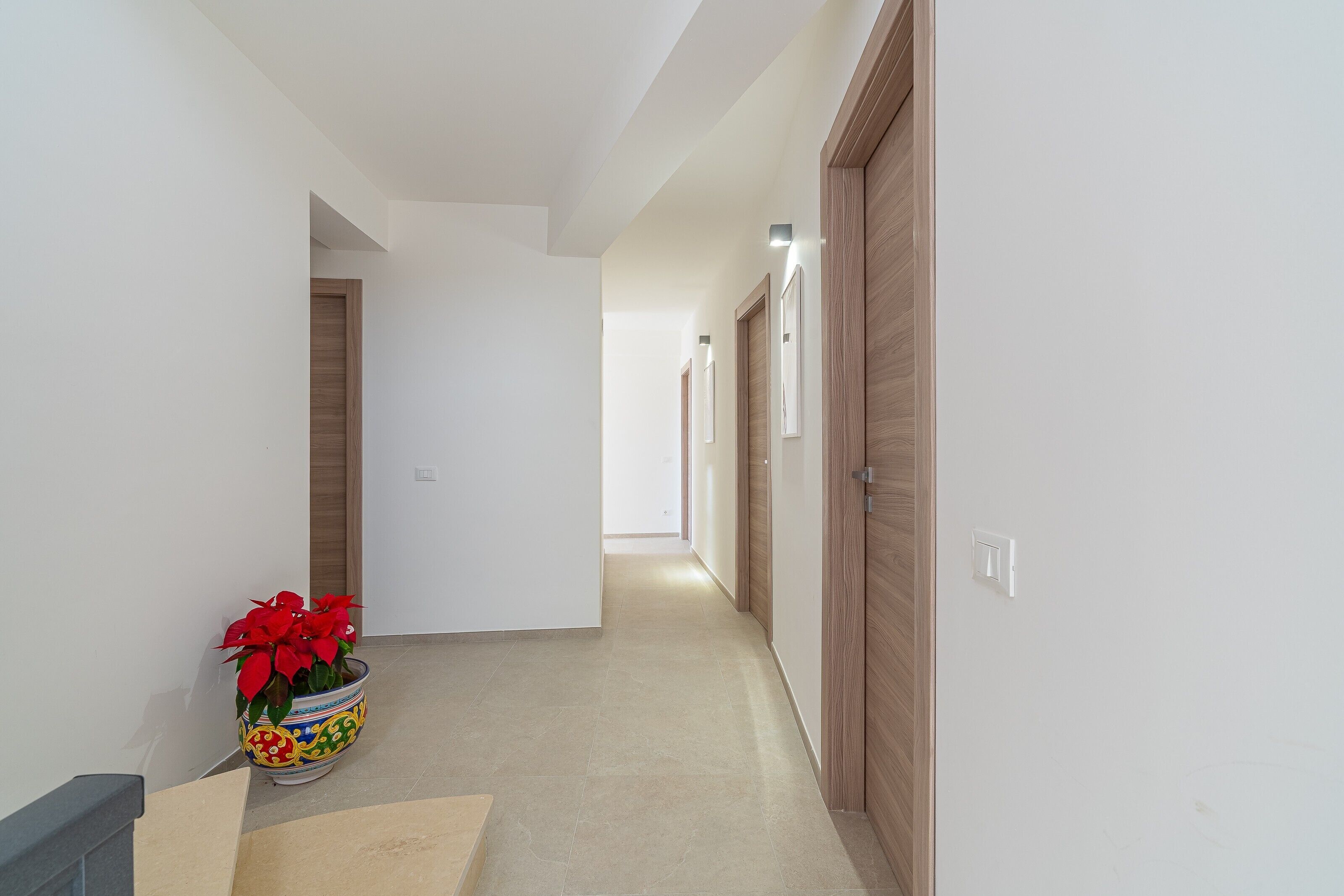 A hallway with a potted plant, wooden doors, and a light switch.