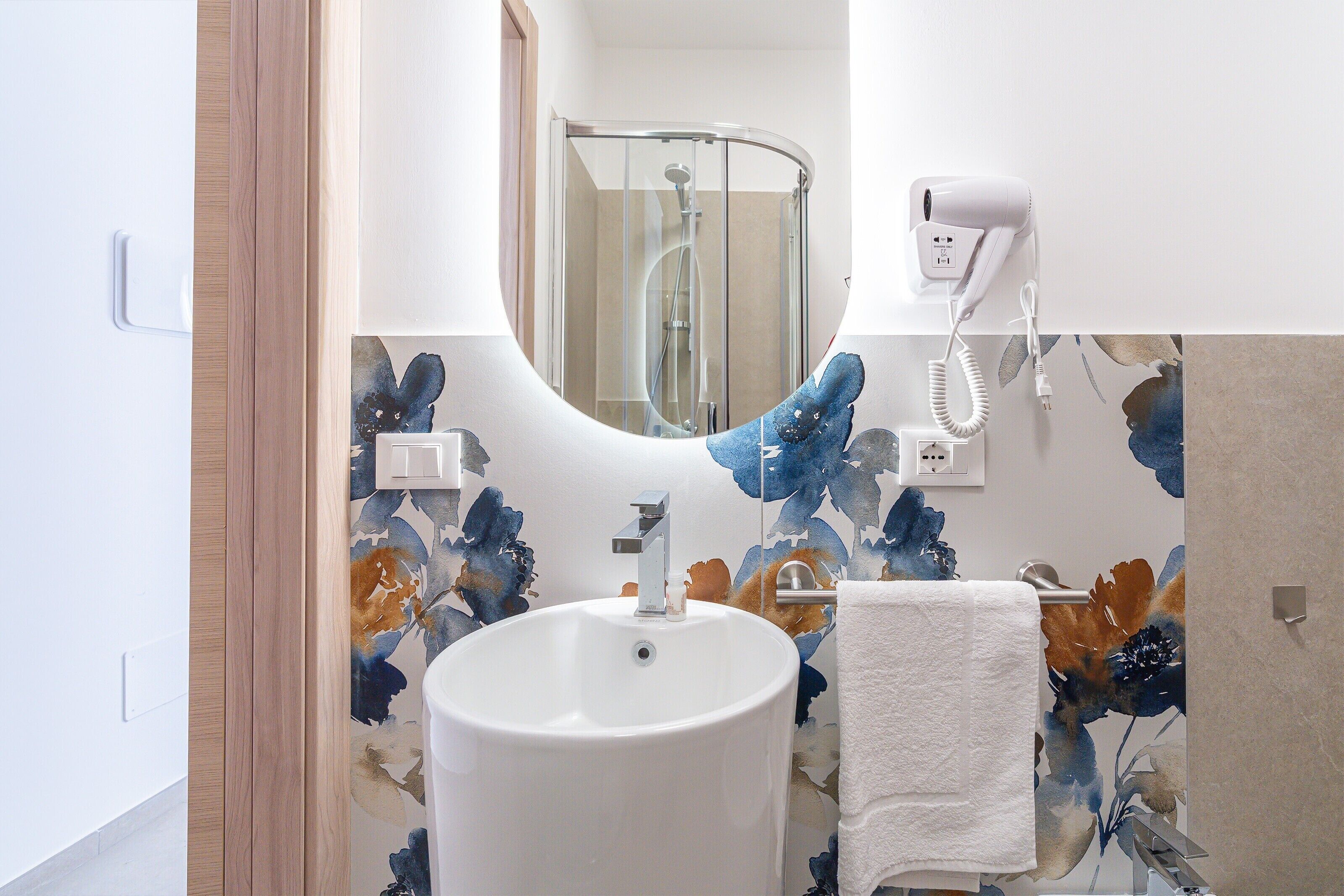 A bathroom with a white sink, a towel hanging on the wall, and a hairdryer mounted on the wall.