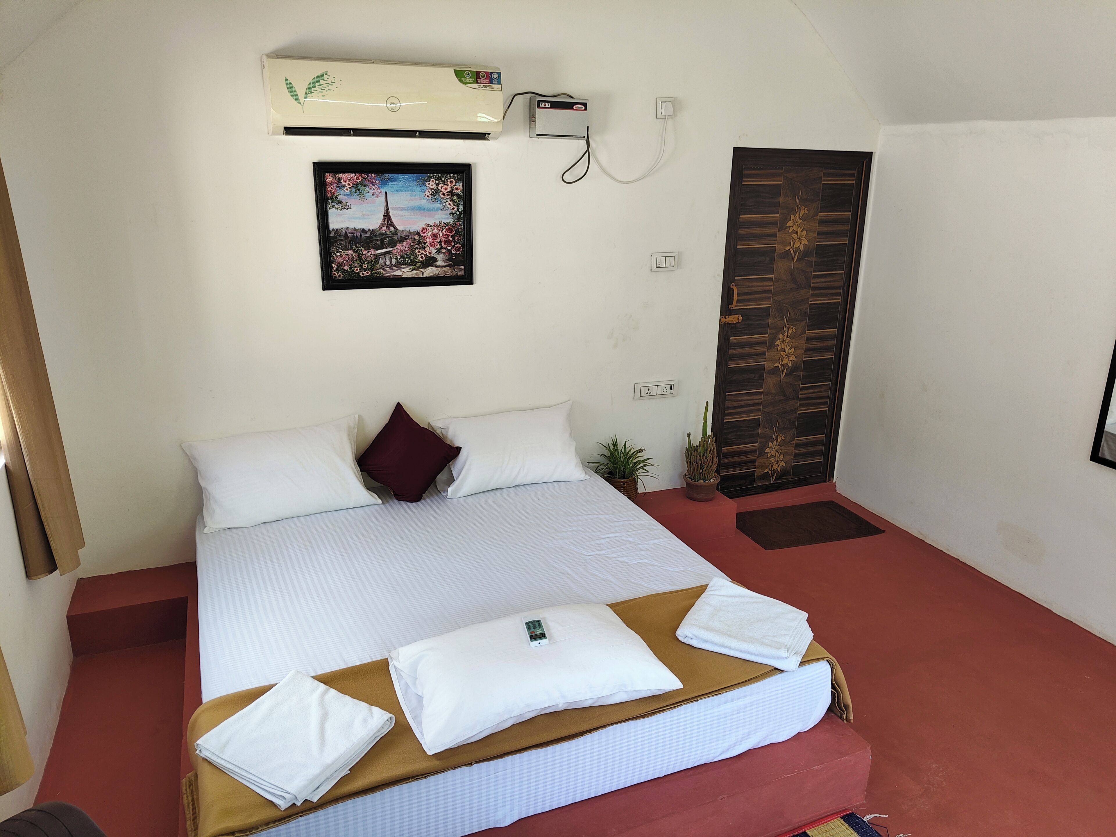 Una cama bien hecha con almohadas y toallas dobladas, un aire acondicionado de pared, un cuadro enmarcado y una puerta con panel decorativo.