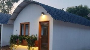 A small, single-story house with a white exterior and a blue tiled roof. It features a wooden door and windows with wooden frames. The house is surrounded by a gravel driveway and has a small garden with various plants. - sree veda wellness resort (Vanur)