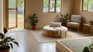 A spacious room with a high ceiling, a round seating area, a sofa, a chair, and several potted plants. - sree veda wellness resort (Vanur)