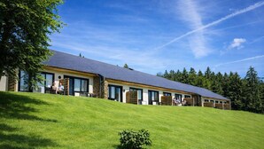 A modern building with a sloped roof, large windows, and a grassy hill in the foreground.