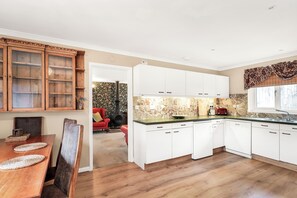 A kitchen with white cabinets, a wooden dining table, and a red chair. - 2-Bed Home with Free Parking - 2 min Walk to Bus (Cambridge)