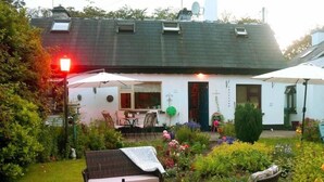 Een gezellig buiten zitgedeelte met rieten meubels en een tafel voor twee, omgeven door een goed onderhouden tuin met diverse planten en bloemen.