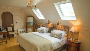 Een slaapkamer met een groot bed, een bureau en een stoel. Er zijn dakramen en een kroonluchter.