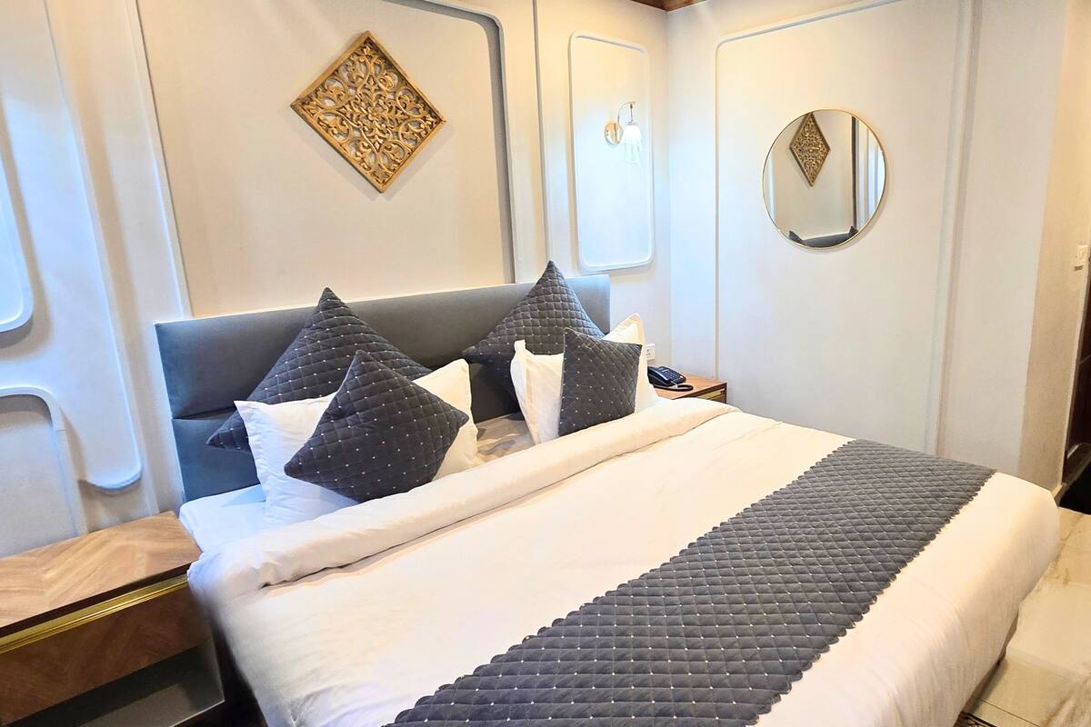 Un lit bien fait, avec une tête de lit matelassée, une table de chevet avec une lampe et des œuvres d’art décoratives accrochées au mur.