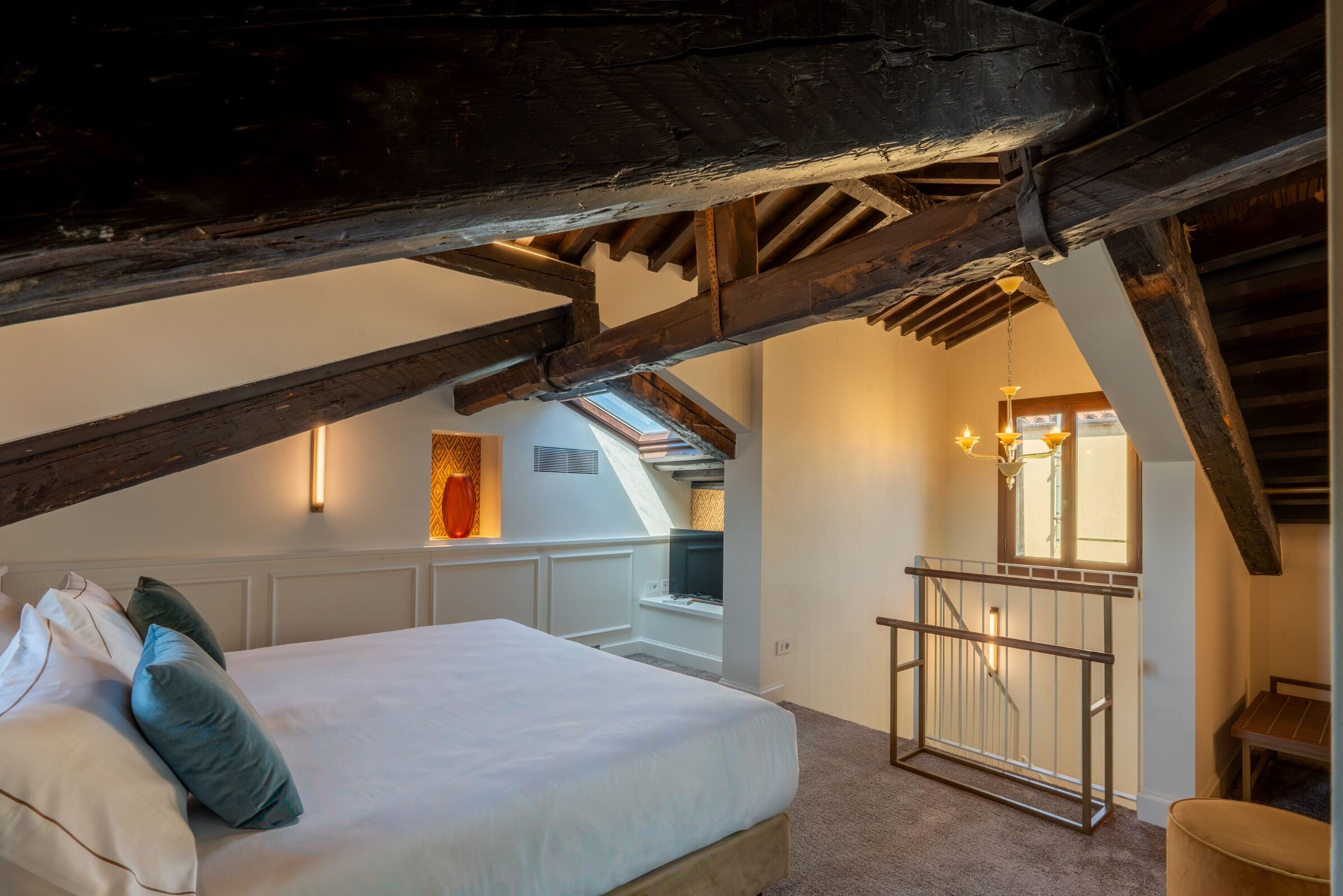 Quarto com cama, almofadas, janela e escada que leva a um andar superior.