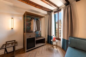 A room with a wooden wardrobe, a small table with a vase, a sofa, and a view of buildings through a window. - Hotel San Samuele (Venice)