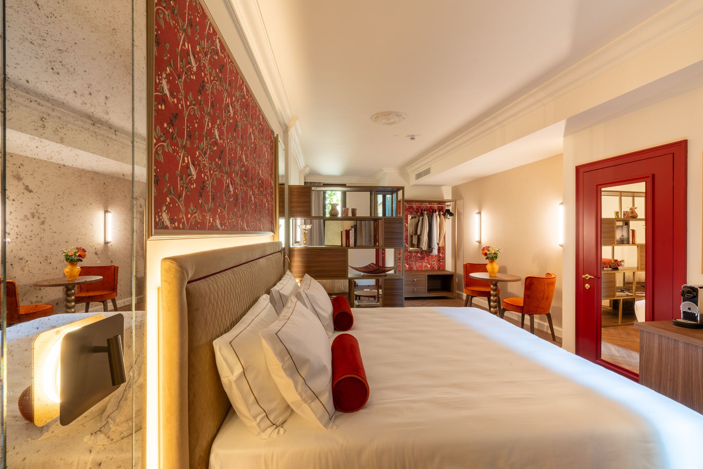 Une chambre d’hôtel avec un grand lit, un coin salon avec des fauteuils, une petite table et une bibliothèque.