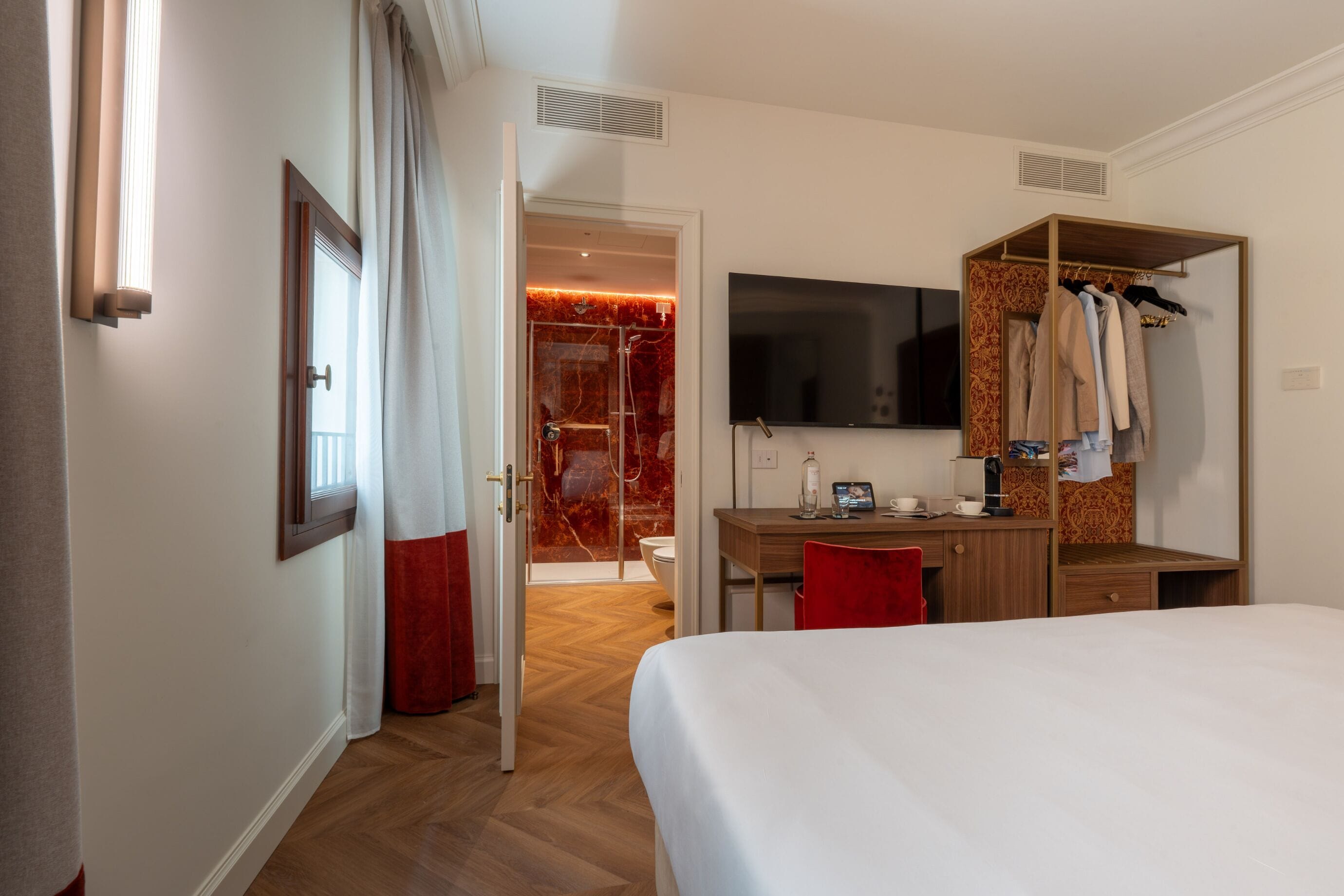A hotel room with a bed, a desk, a TV, a wardrobe, and a shower area.