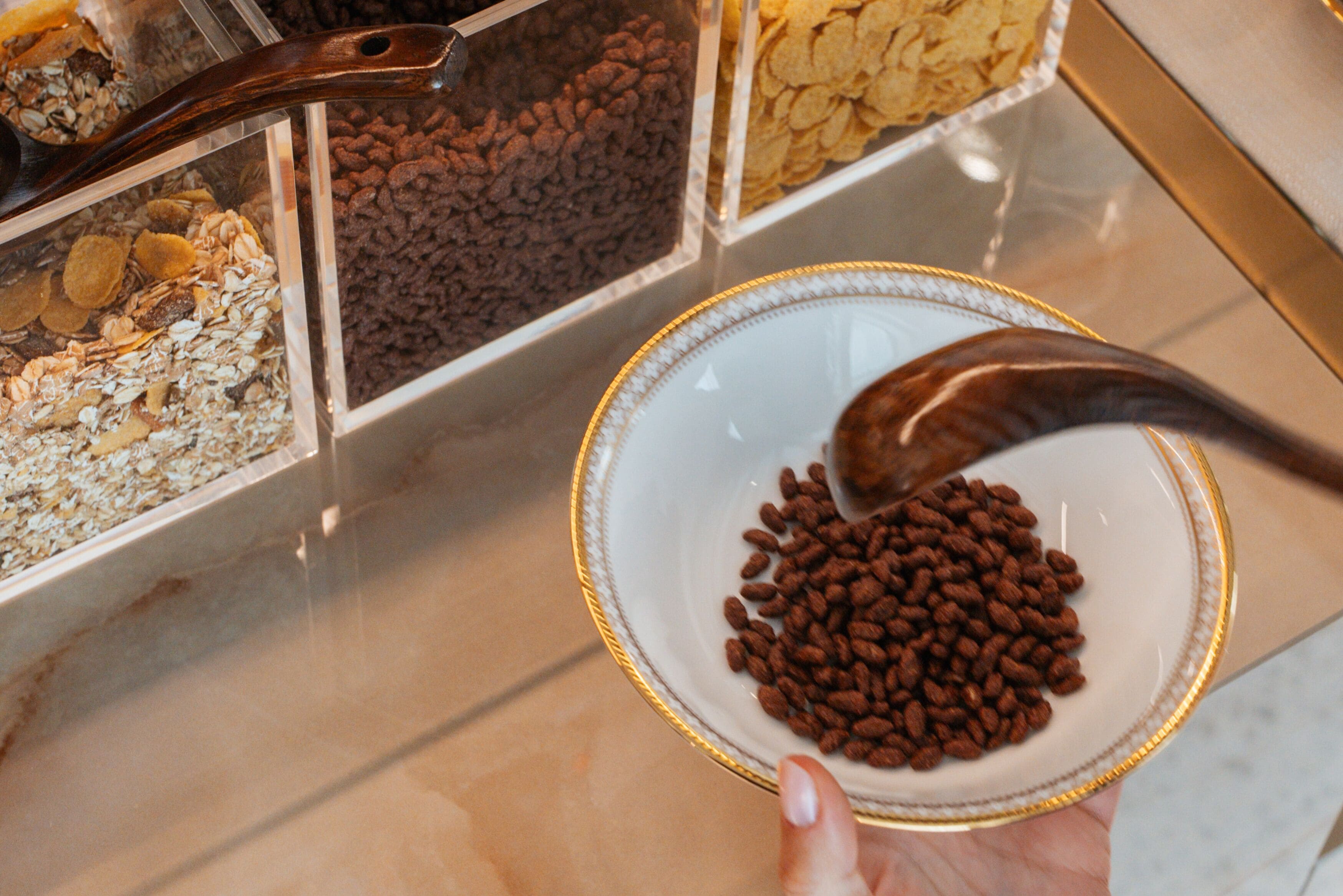 A hand holding a bowl with a spoonful of brown pellets, with various food containers in the background.