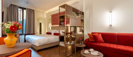 Une chambre d’hôtel avec un lit, un canapé rouge, une petite table, un miroir et un meuble décoratif.