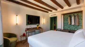 A hotel room with a large bed, a desk with a chair, a mirror, and a wardrobe with hanging clothes.